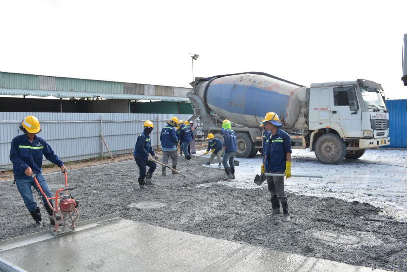 Workers levelling a fresh concrete slab with a transit mixer behind